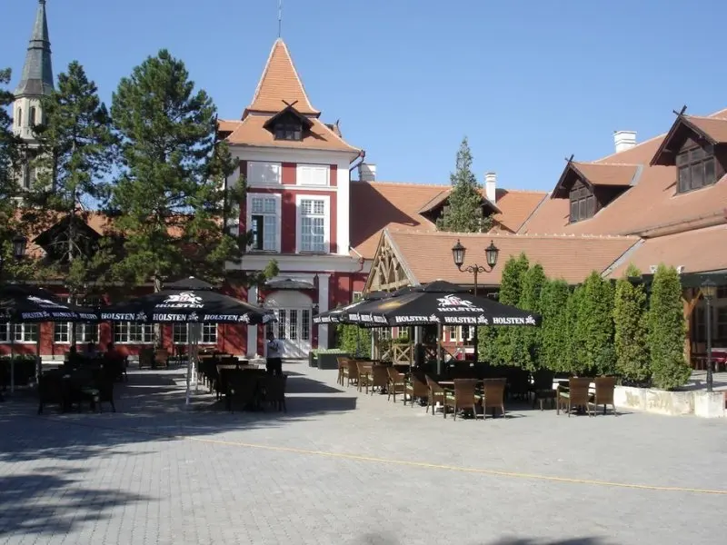 Dvorište sa terasom u Lovačkom Dvorcu Kaštel Ečka sa crnim suncobranima, stolovima i stolicama, tornjem i drvenim krovovima