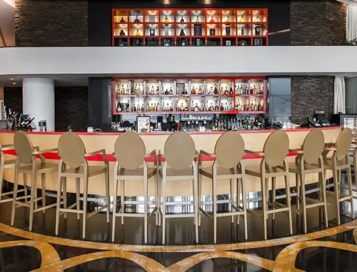 Bar sa šankom u Hotel Splendid Conference & Spa Resort sa visokim bež stolicama, osvetljenim policama sa pićima, crvenim akcentima i mermernim podom