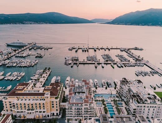 Aerial pogled na Regent Porto Montenegro i marinu u zalazak sunca sa žutom fasadom hotela, bazenima, jahtama i Bokokokotorskim zalivom