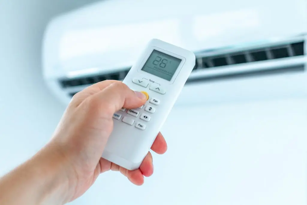 indoor air quality solutions hand holding controller Air conditioner temperature adjustment with remote controller in room at home.