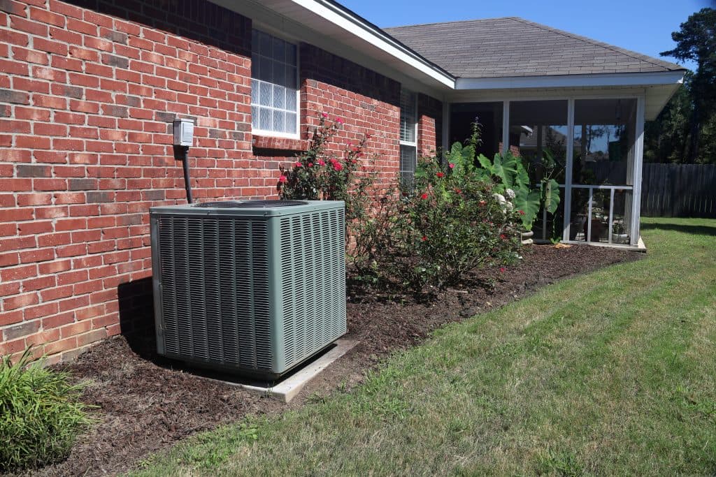 hvac warranty Air Conditioner system next to a home, modern clean with bushes and brick wall