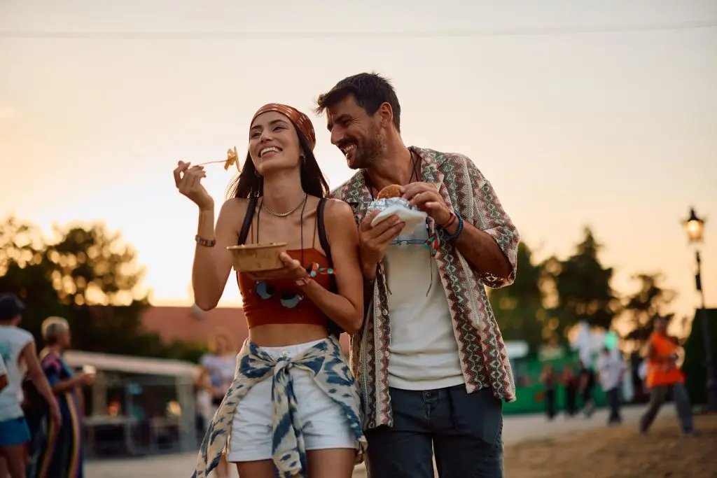 Happy couple eating while attending summer music festival at sunset. Copy space.Happy couple eating while attending summer music festival at sunset. Copy space.