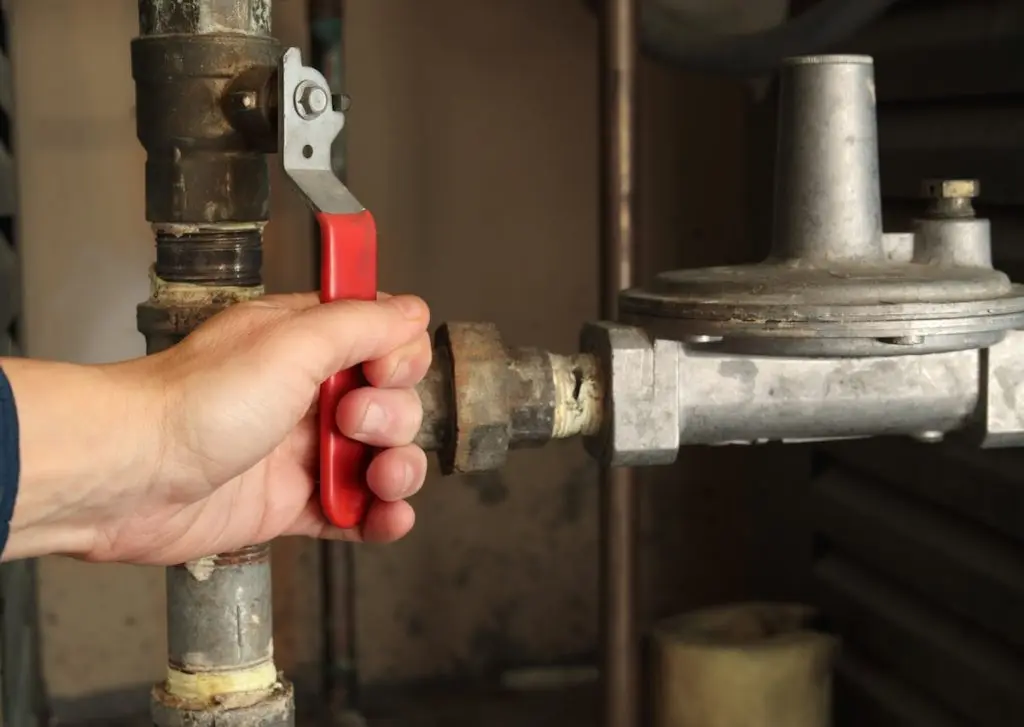 Technician using shut-off valve in front of gas pressure regulator. Natural gas boiler supply line for hot water heating. Gas safe, technician or plumbing hot water background. Selective focus.