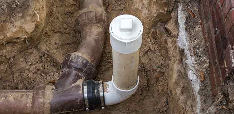 Sewer line repair showcasing new white PVC pipe connected to existing black pipes in excavated trench, emphasizing Force Plumbing and Heating LLC's services in Holmdel, New Jersey.