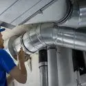 Technician repairing ductwork in a mechanical room, showcasing professional plumbing and HVAC maintenance.
