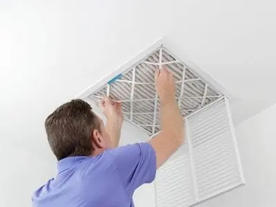 Man replacing air filter in ceiling vent for HVAC maintenance, emphasizing importance of air quality and system efficiency.