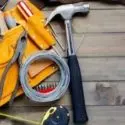 DIY tools for plumbing and HVAC: hammer, pliers, measuring tape, and orange tool belt on wood surface.