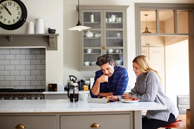 Young couple using a digital tablet while sitting at their kitchen table at home
