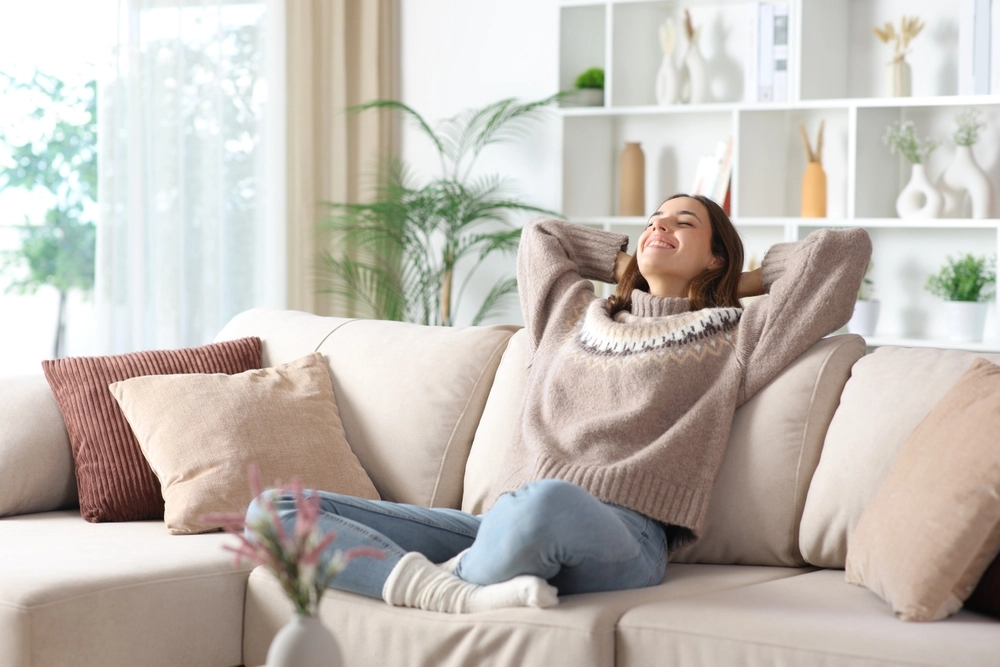 Happy woman in winter relaxing and breathing sitting on a sofa at home