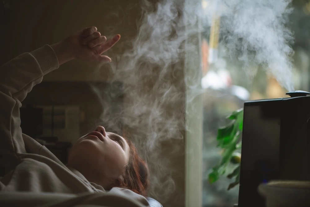 Teen girl lying on a sofa, pointing at vapor from a humidifier