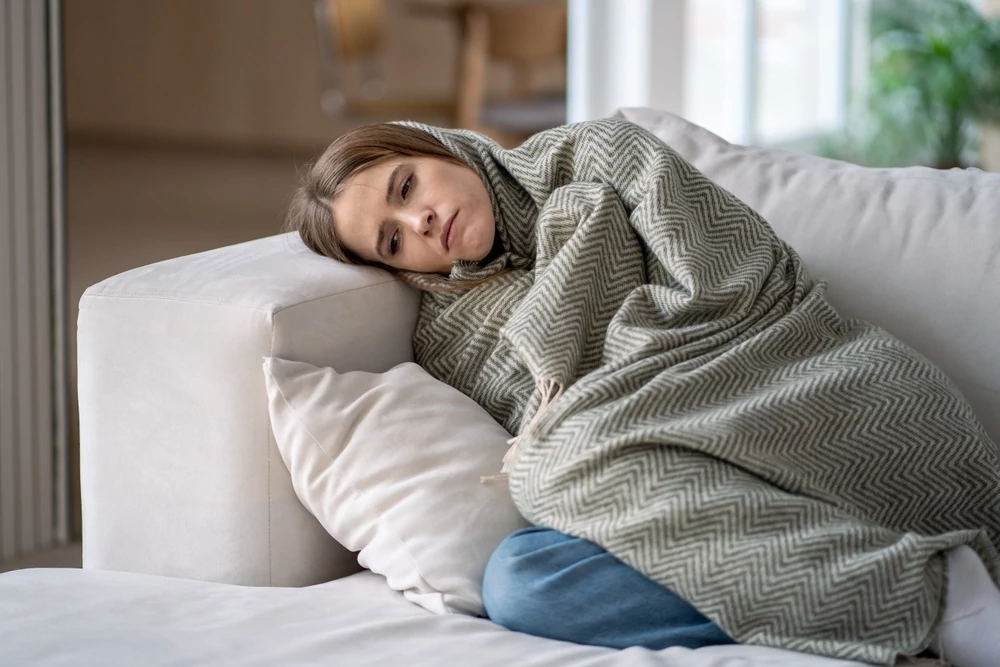 Woman lying on couch covered by blanket