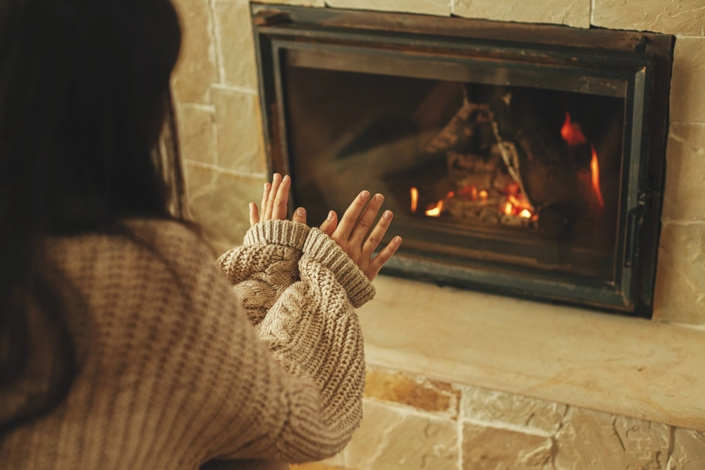 Woman putting her hands next to an indoor fireplace