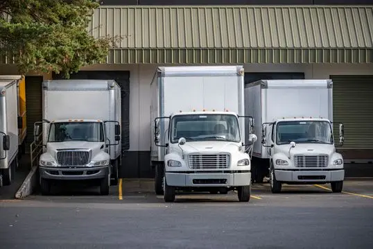 Useful Industrial standard for local deliveries and short haul freights compact middle duty rigs semi trucks with box trailers standing in warehouse dock with gates loading cargo for next delivery