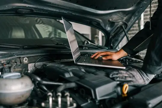 A mechanic using a laptop on a car engine for diagnostics in a garage. Highlights the use of technology in modern vehicle maintenance and repair.