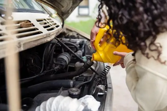 Millennial woman putting oil in vintage camper van. She is casually dressed with warm clothes. Horizontal close-up outdoors shot with copy space. No face. This is part of a series and was taken in Montreal, Quebec, Canada.