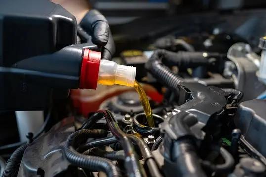 Close-up of engine oil being poured into a modern car engine during a maintenance procedure.