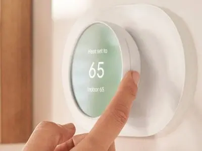 Person adjusting a smart thermostat displaying a heat setting of 65 degrees, illustrating energy monitoring and HVAC efficiency.