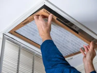 Person replacing air filter in ceiling HVAC system to maintain heater efficiency and improve indoor air quality.