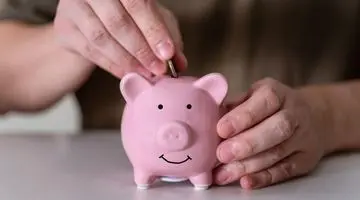 Person inserting coin into a pink piggy bank, symbolizing saving money while maintaining home comfort and reducing air conditioning costs.