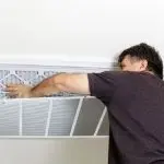HVAC technician replacing air filter in ceiling vent during maintenance visit for improved system reliability and indoor air quality.