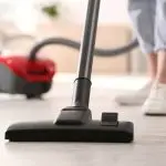Vacuum cleaner nozzle on hardwood floor with person in casual attire, emphasizing home cleaning for improved indoor air quality and HVAC efficiency.