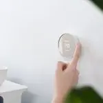 Person adjusting a modern thermostat on a wall, showcasing temperature control for effective air conditioning in a home setting.