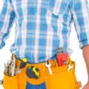 HVAC technician wearing a plaid shirt and tool belt with various tools, symbolizing hands-on skills needed for a career in HVAC services.