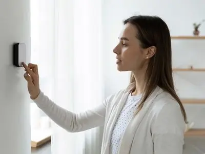 Woman adjusting a smart thermostat on the wall, emphasizing the importance of accurate temperature readings for effective HVAC management.
