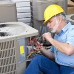 Air conditioning repair technician working on outdoor AC unit, checking wiring and components, demonstrating maintenance expertise relevant to HVAC services.