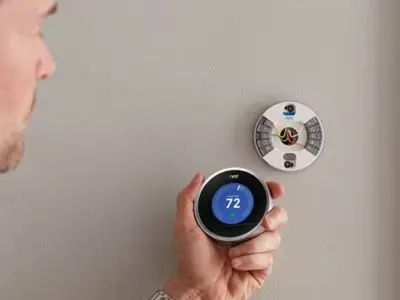 Person adjusting a smart thermostat displaying a temperature of 72 degrees, illustrating energy efficiency and remote control capabilities for HVAC systems.