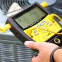 Technician using a digital thermometer to assess air conditioning unit performance, highlighting HVAC maintenance and service.