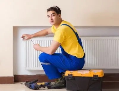 HVAC technician in blue overalls working on a heater, with tools and a toolbox nearby, illustrating professional maintenance and repair services.
