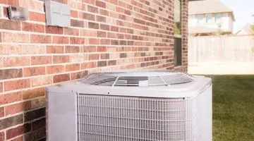 Air conditioning unit installed outside a home, adjacent to a brick wall, representing essential HVAC solutions for residential comfort.