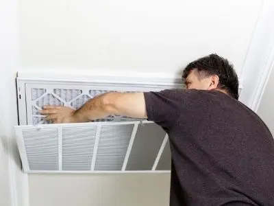 Man replacing an air filter in an HVAC system, emphasizing the importance of regular maintenance for optimal performance and indoor air quality.