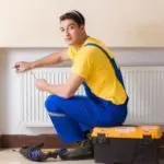 HVAC technician in blue overalls performing maintenance on a radiator, emphasizing heating system efficiency and service expertise.