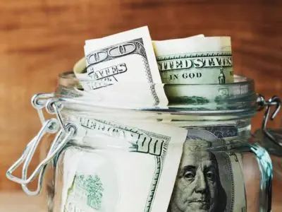 Jar filled with U.S. dollar bills, symbolizing savings and lower utility costs from efficient air conditioning maintenance during summer.