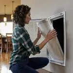 Woman replacing air filter in home HVAC system, promoting indoor air quality and efficient air conditioning maintenance.