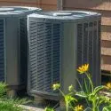 Air conditioning units installed outdoors, surrounded by green foliage, representing HVAC solutions for home cooling needs.