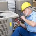 HVAC technician in a hard hat repairing an air conditioning unit, illustrating maintenance tips for homeowners.