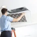 Air conditioning repair professional inspecting and replacing an air filter in a ceiling-mounted AC unit, emphasizing maintenance for optimal system functionality.