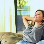 Woman relaxing on a couch, enjoying a comfortable indoor environment, illustrating the benefits of smart thermostats and HVAC services for home comfort.