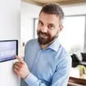 Man adjusting a digital thermostat in a modern home, emphasizing HVAC efficiency and temperature control for optimal comfort.