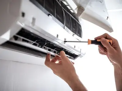 Hands using a screwdriver to service a ductless mini-split air conditioning unit, illustrating easier installation and maintenance compared to traditional ducted systems.