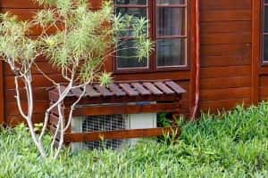 Air conditioning unit partially shaded by wooden slats and surrounded by grass, illustrating sun protection for HVAC systems.