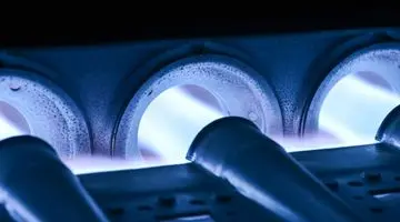 Close-up of a furnace burner assembly with blue flames, illustrating components relevant to furnace overheating and maintenance.