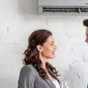 Woman and man smiling near air conditioning unit, discussing HVAC tips for summer comfort.