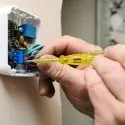 Person using a screwdriver to install or repair a thermostat, highlighting HVAC maintenance for energy efficiency and comfort.