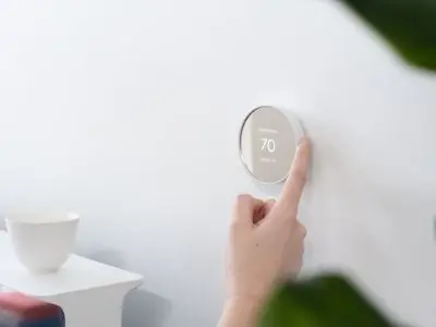 Person adjusting a digital thermostat set to 70 degrees Fahrenheit, illustrating thermostat functionality in HVAC maintenance context.