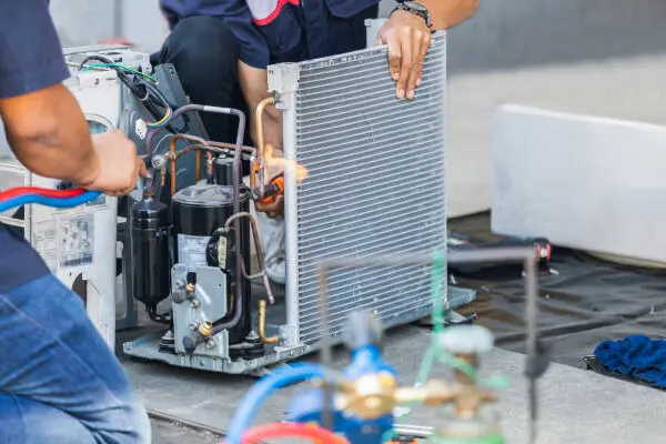 Technicians repairing an air conditioning unit with tools and gauges.