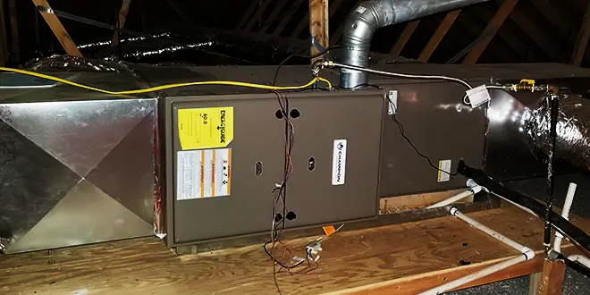 HVAC unit installed in an attic, with visible ductwork and wiring on a wooden platform.